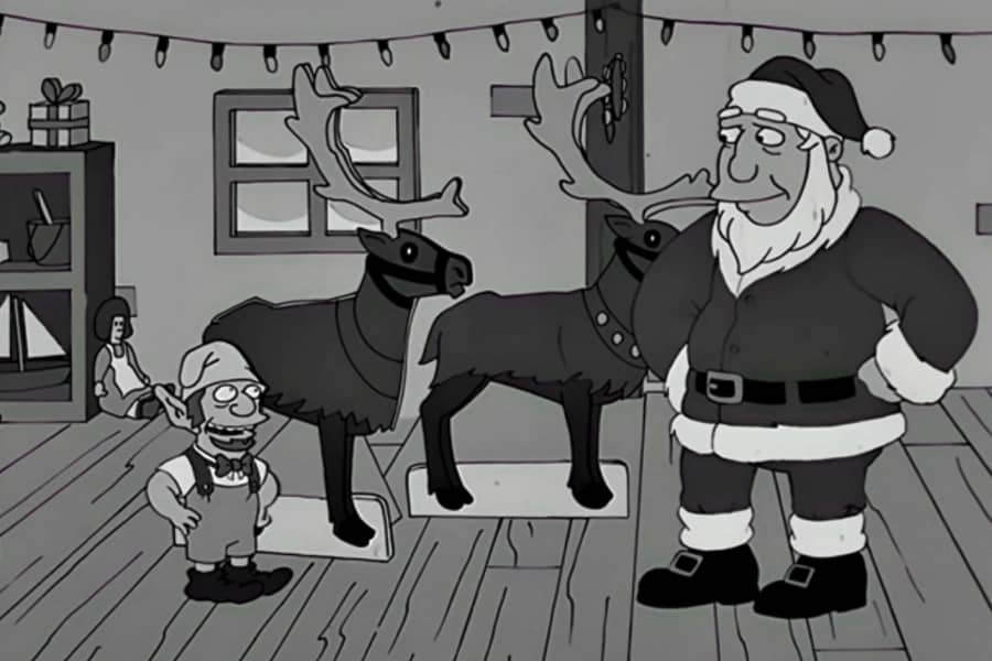 Santa talks with an elf next to two reindeer cardboard cutouts