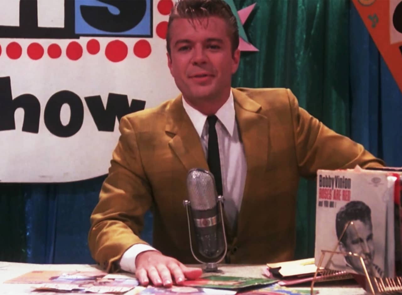 Corny Collins in front of his microphone with a stack of records nearby
