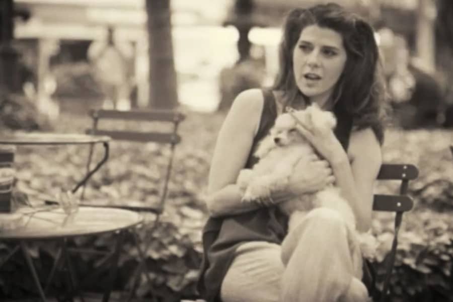 Marisa Tomei sits at a cafe table in the park, holding a small lap dog