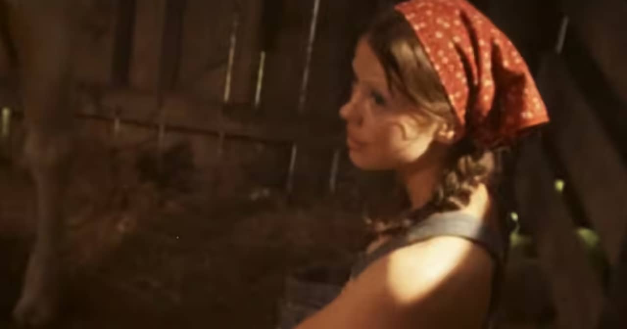 young woman wearing overalls and bandana milking a cow