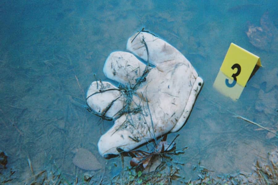 a crime scene photo of a large white Goofy glove laying in dirty water