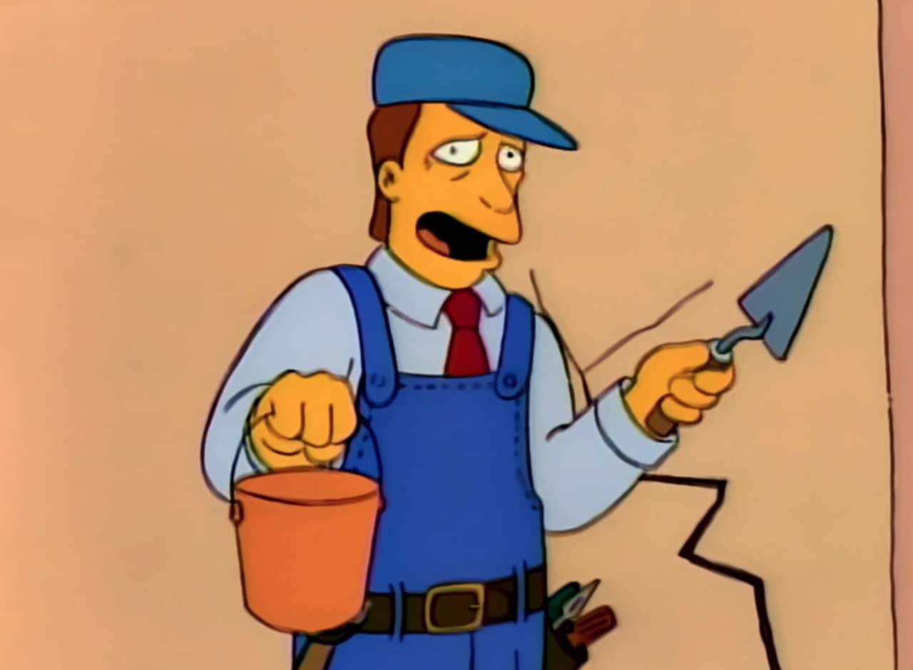Troy McClure wearing overalls, holding a bucket and trowel, in front of a crack in the wall