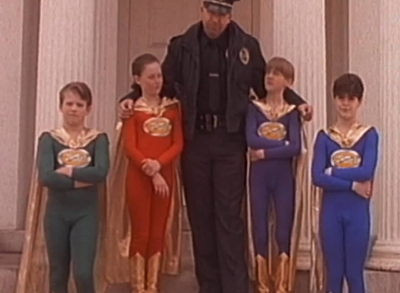four kids (the Junior Defenders) in superhero costumes with a police officer