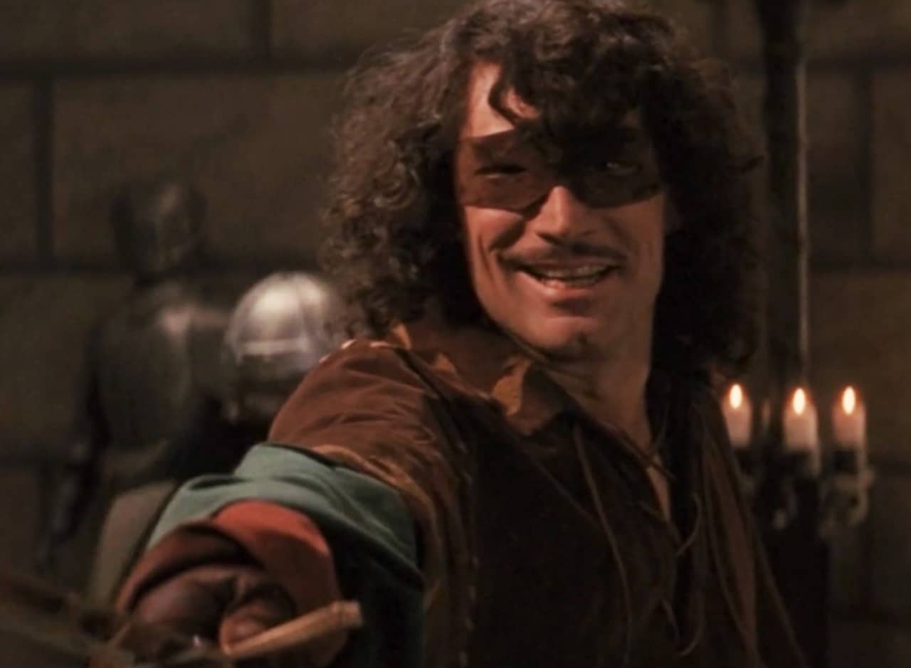 a heroic man in a mask grins while holding a sword