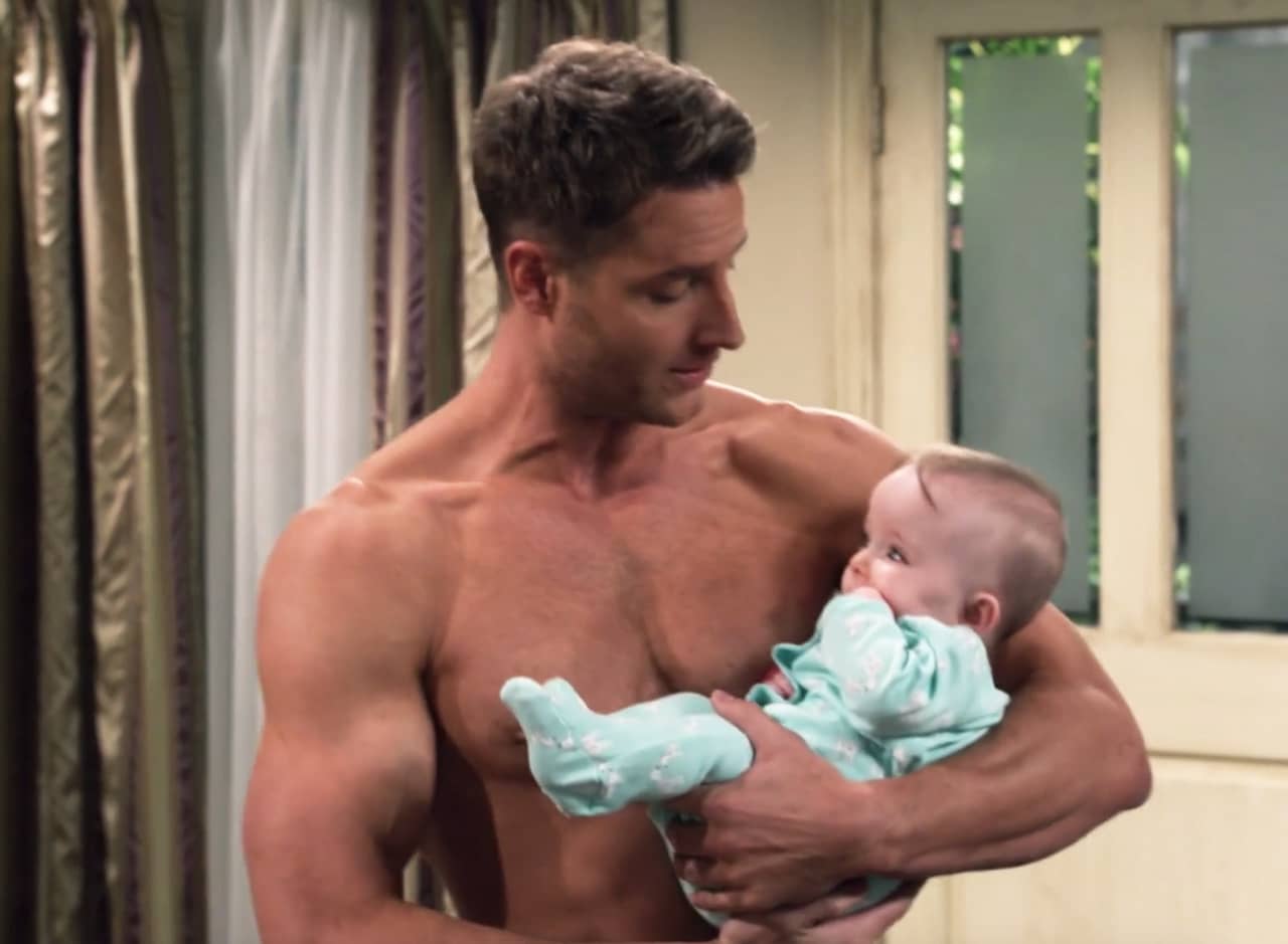 a shirtless Kevin Pearson holds a baby