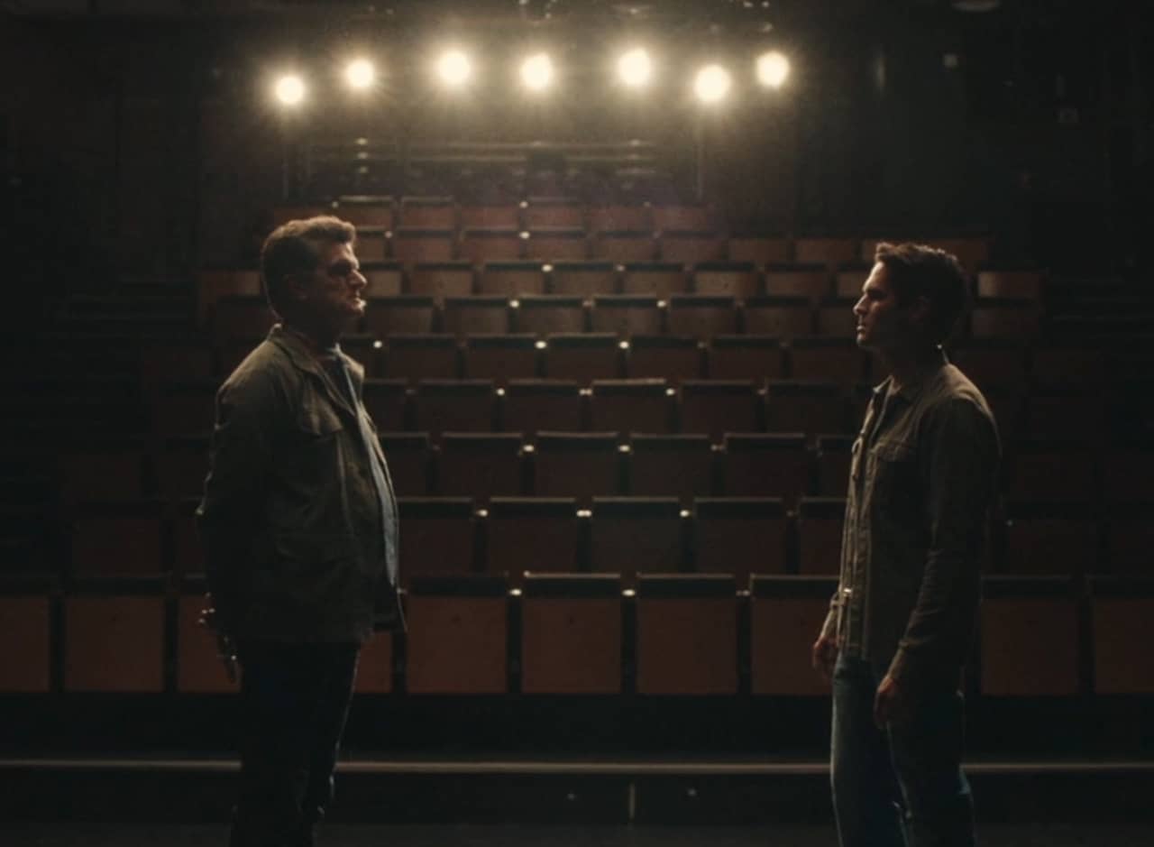 two men stand on a dark stage looking at each other