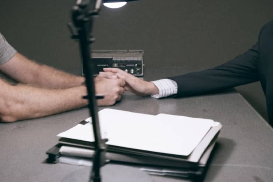 across an interrogation table, a boy’s hand reaches out and touches a man’s hand