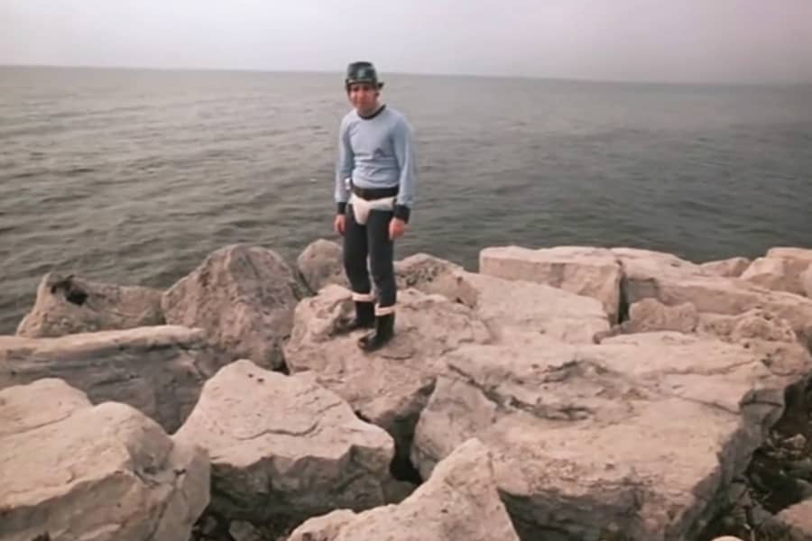 Doug standing on some rocks by the water, wearing a helmet and underwear over his pants