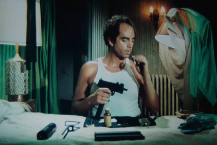 Roark cleaning a gun on a hotel bed