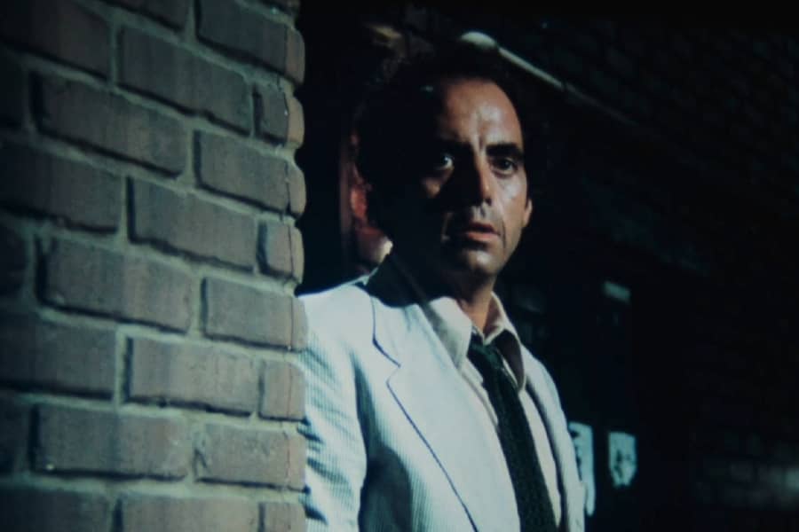 Roark in a suit next to a brick wall