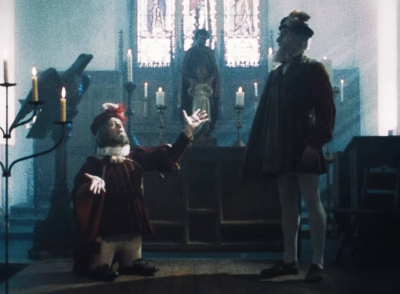 in an old candle-lit church, Aldo Vacci is a dwarf talking to a taller man