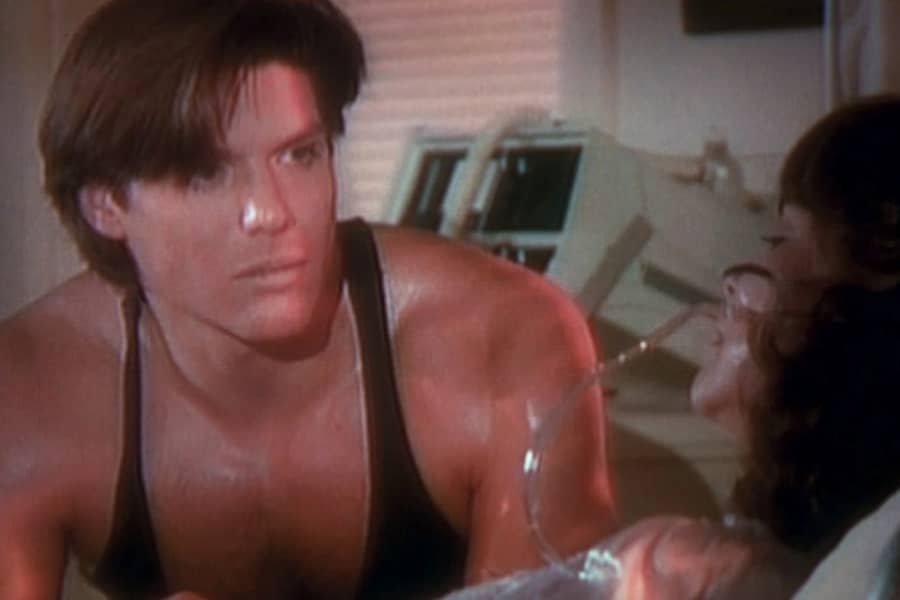 Blair Brennan as Bolt in a tank top, at Maggie’s hospital bed