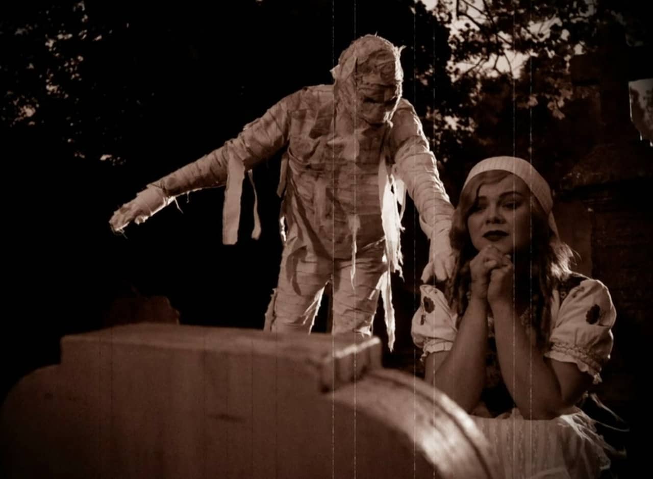 mummy approaching a woman praying at a gravestone