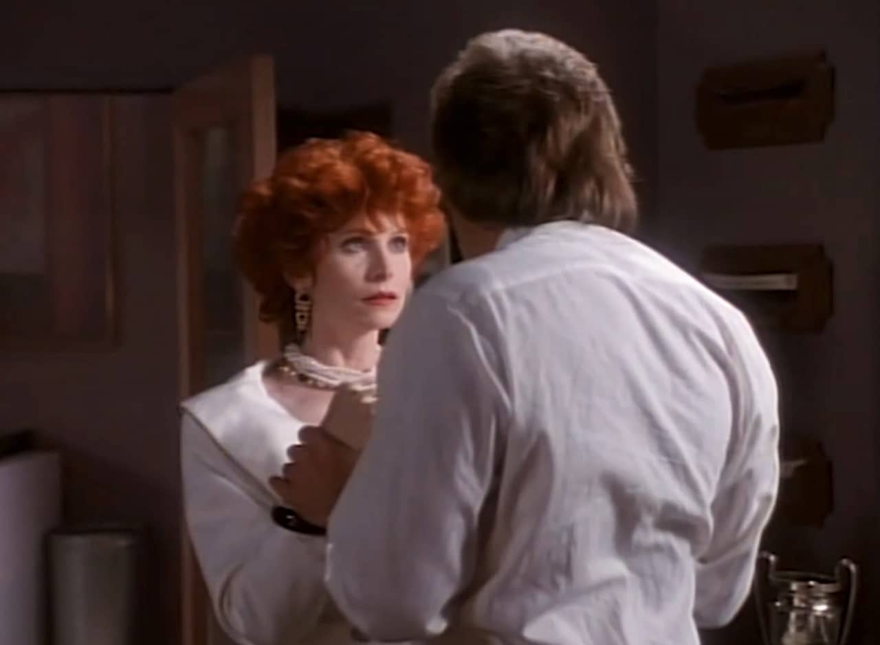 Fuschia, a red-haired professional woman, talking with her boss, Evian, who is holding her wrists