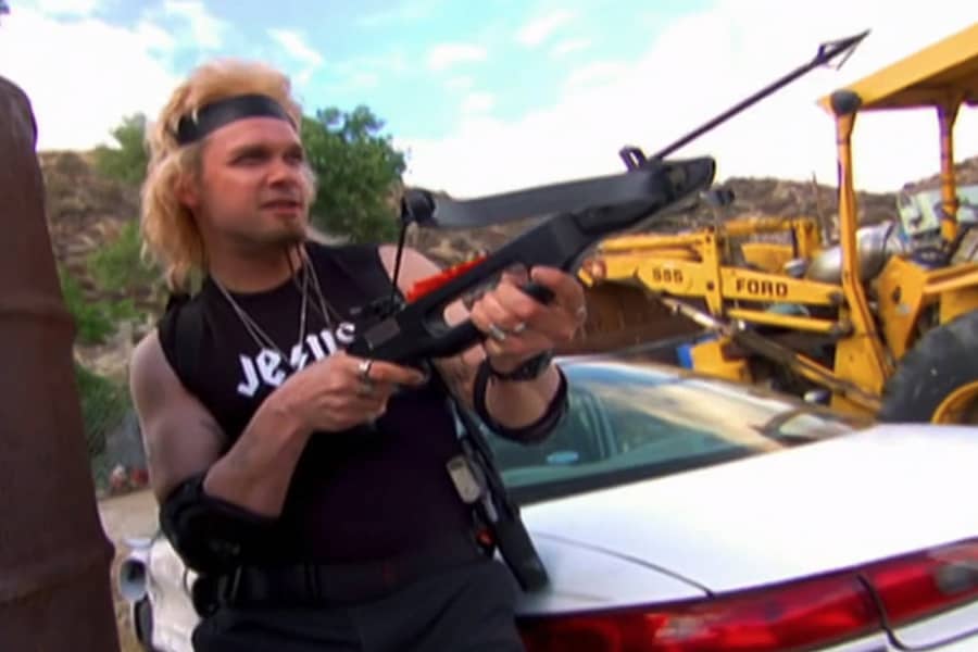 Tommy aiming a crossbow in a junkyard