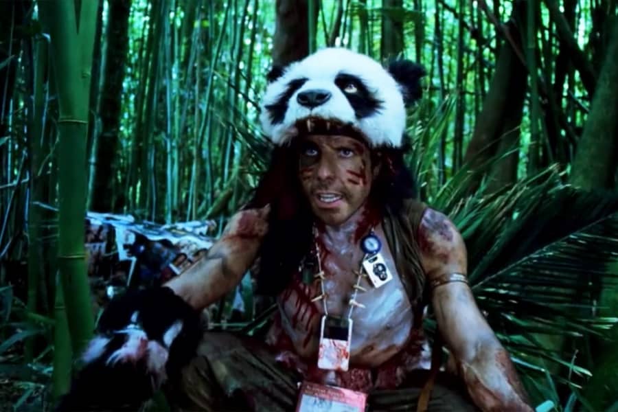 Speedman shirtless and covered in dirt and bloody warpaint, wears a panda’s head as a hat