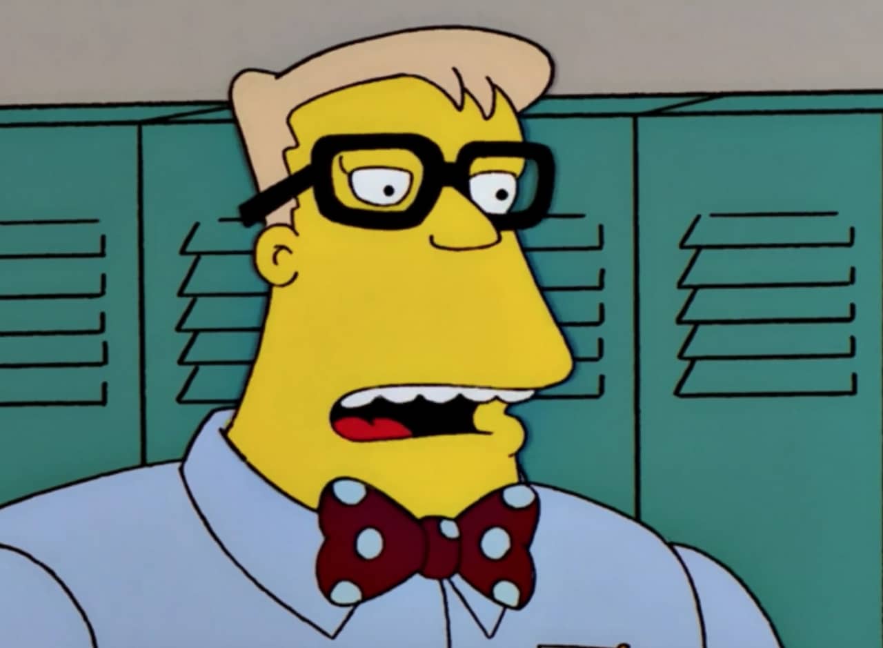 Rainier Wolfcastle in a high school wearing a bowtie and thick black glasses