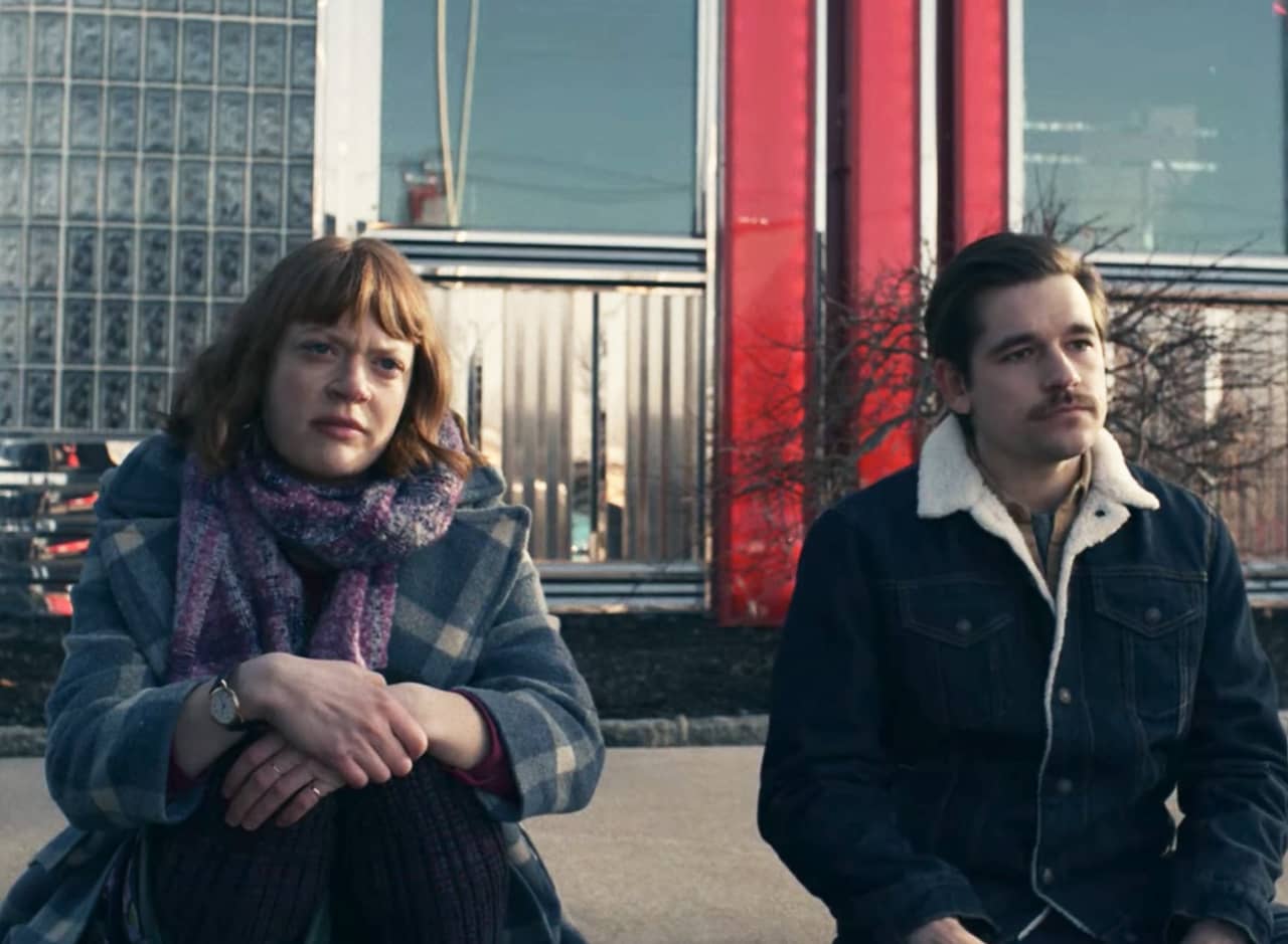 a young man and woman sit solemnly on the curb outside a diner