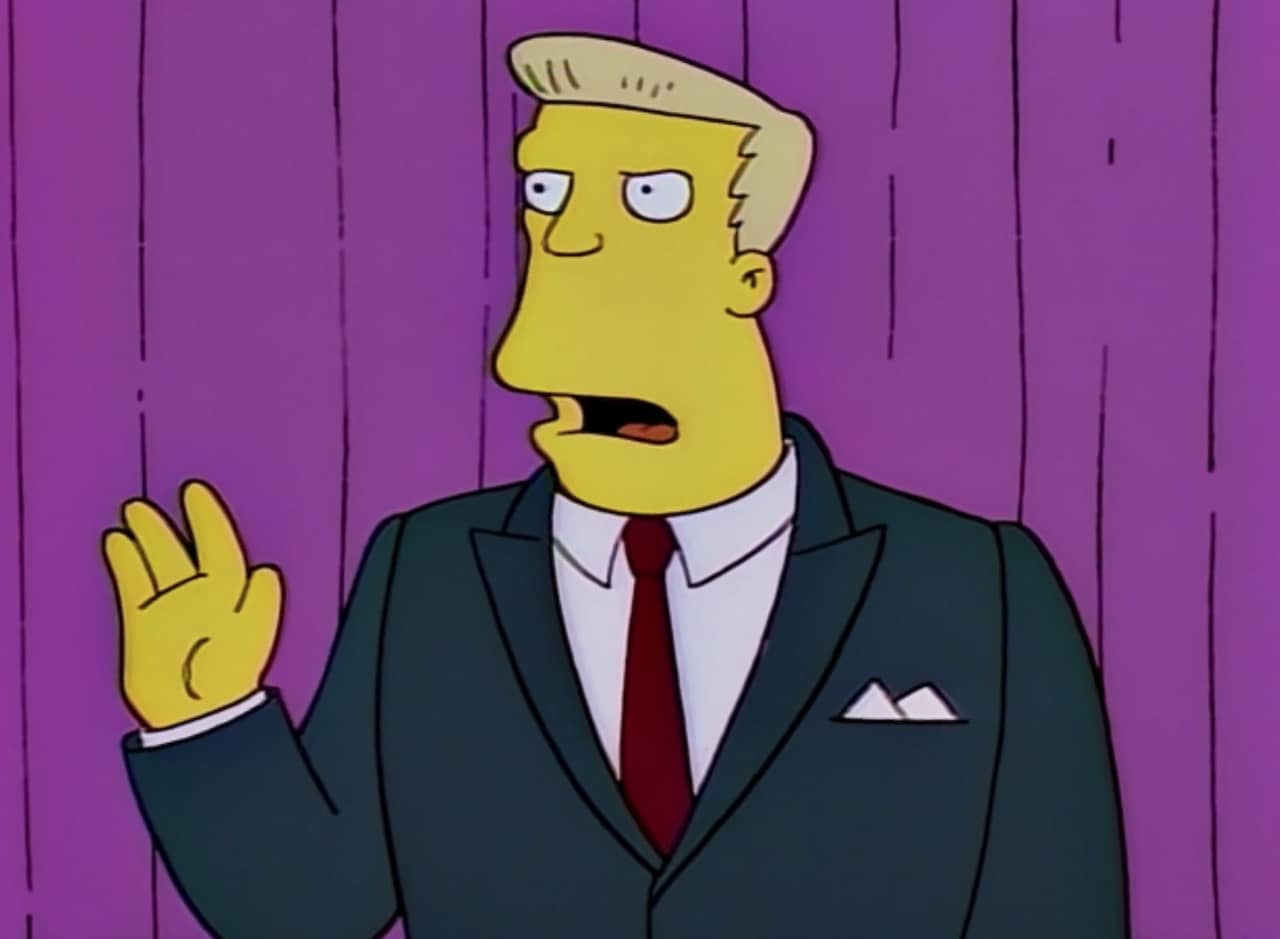 McBain in a suit, in front of a curtain