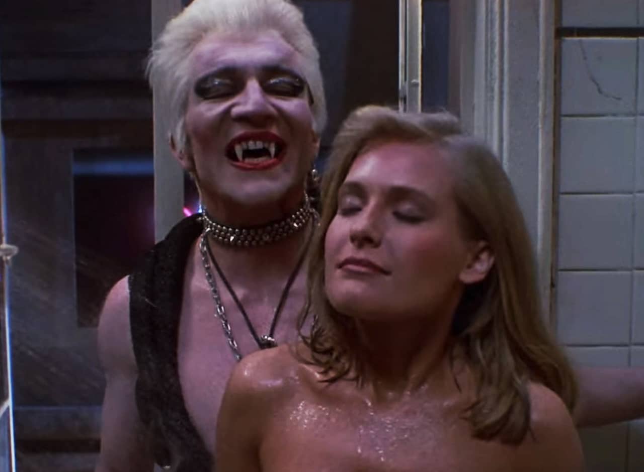 blonde, punk male vampire stands behind a woman in the shower