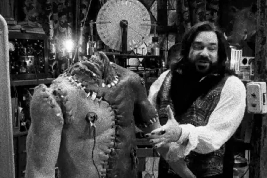 Laszlo stands next to a headless Frankenstein’s monster-esque body of sewn together parts