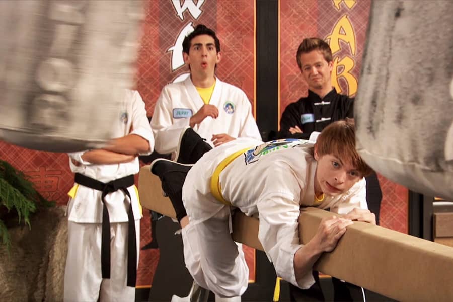 karate kid clinging to a beam as heavy bags swing around him