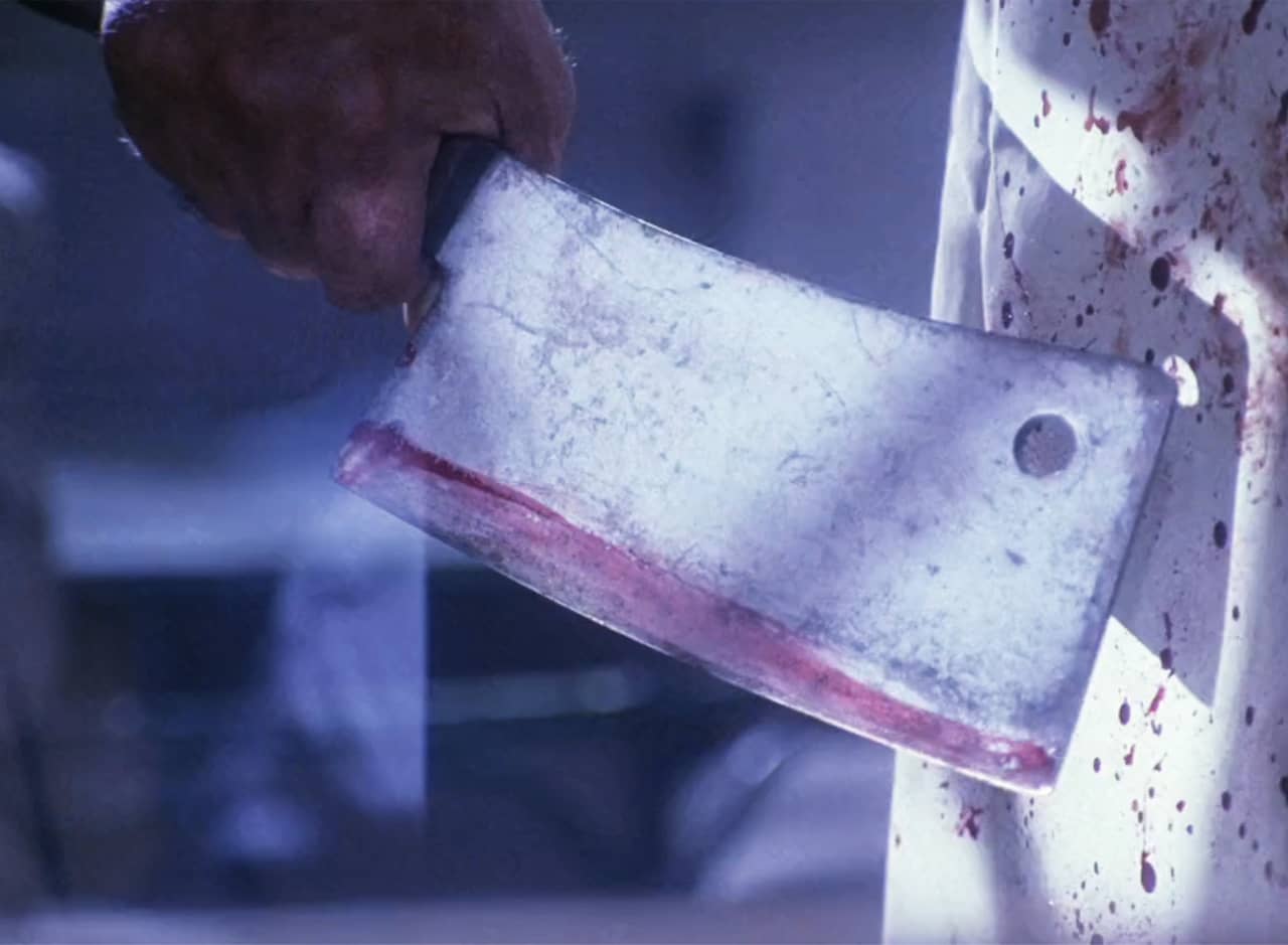 hand holding a butcher knife next to a bloody apron
