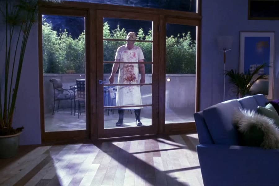 The Butcher, a man in a mask and bloody apron, standing outside a glass front door at night