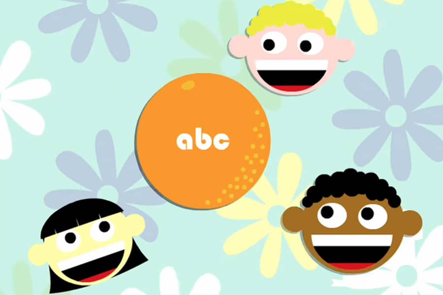 paper cutout faces of three kids, and an orange with the letters “abc” on it