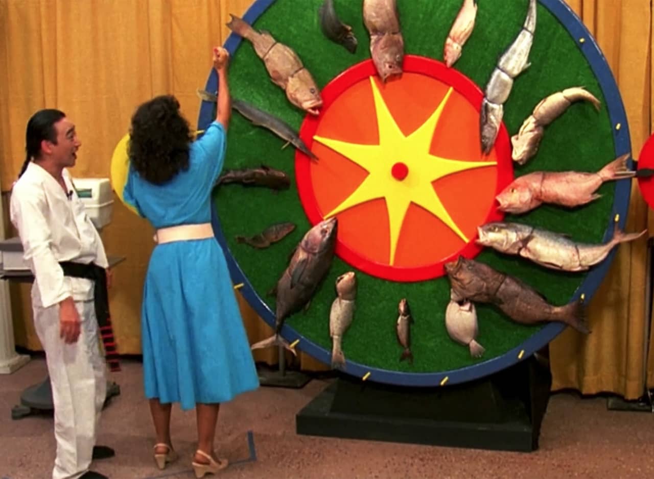a woman reaches up to spin big game show wheel that is covered in various fish