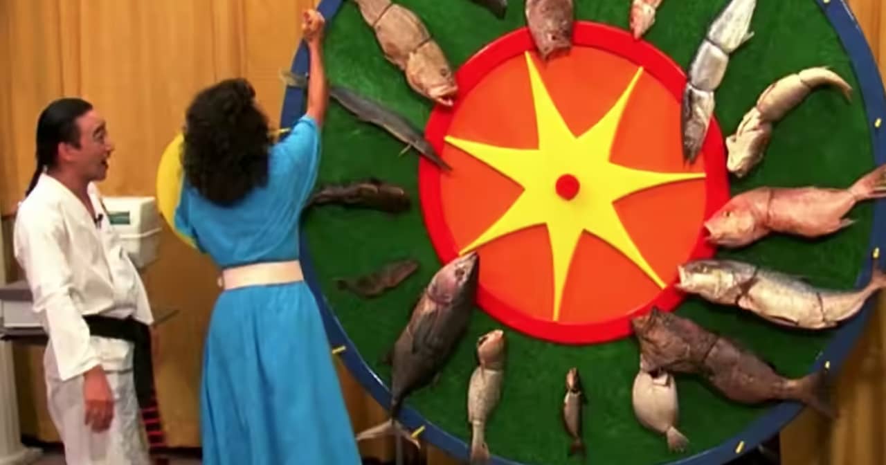 a woman reaches up to spin big game show wheel that is covered in various fish