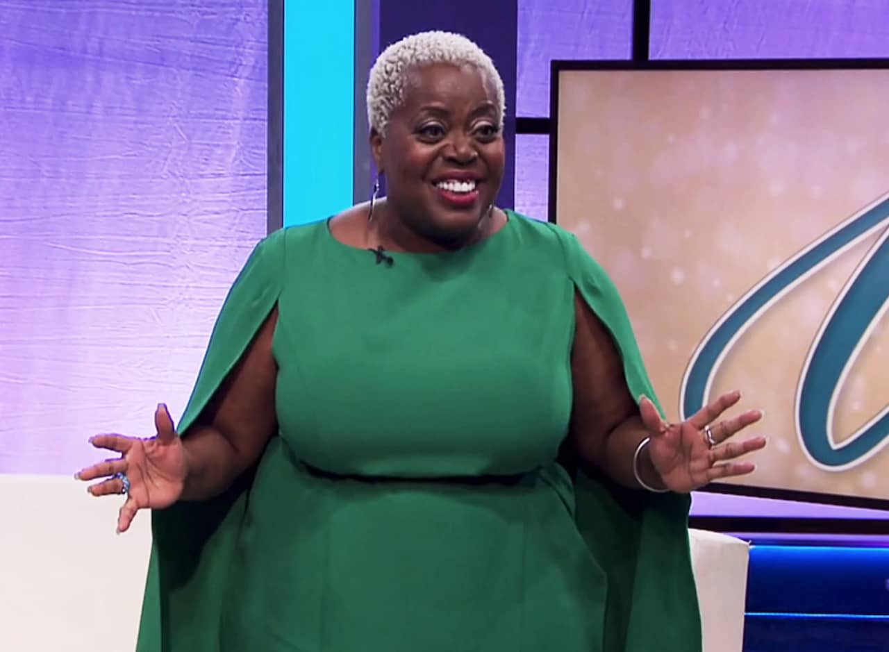 Wilma, a black woman with short white hair wearing a green caped dress