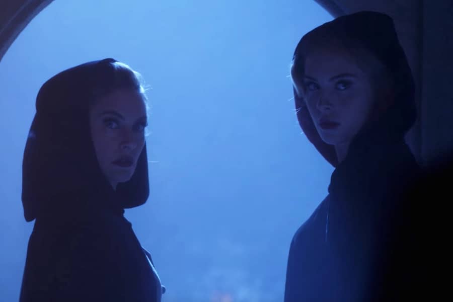 two cloaked women against a backlit night