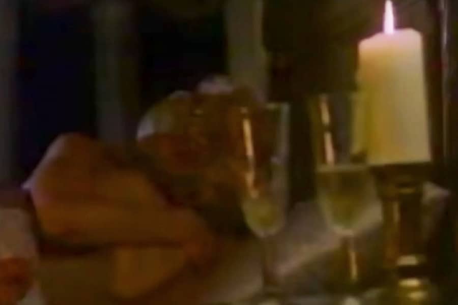 woman and man in bed, a lit candle and glasses of wine on the nightstand
