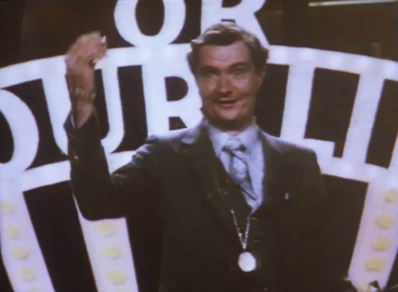 host Jim Broadbent makes the moolah sign with his hand