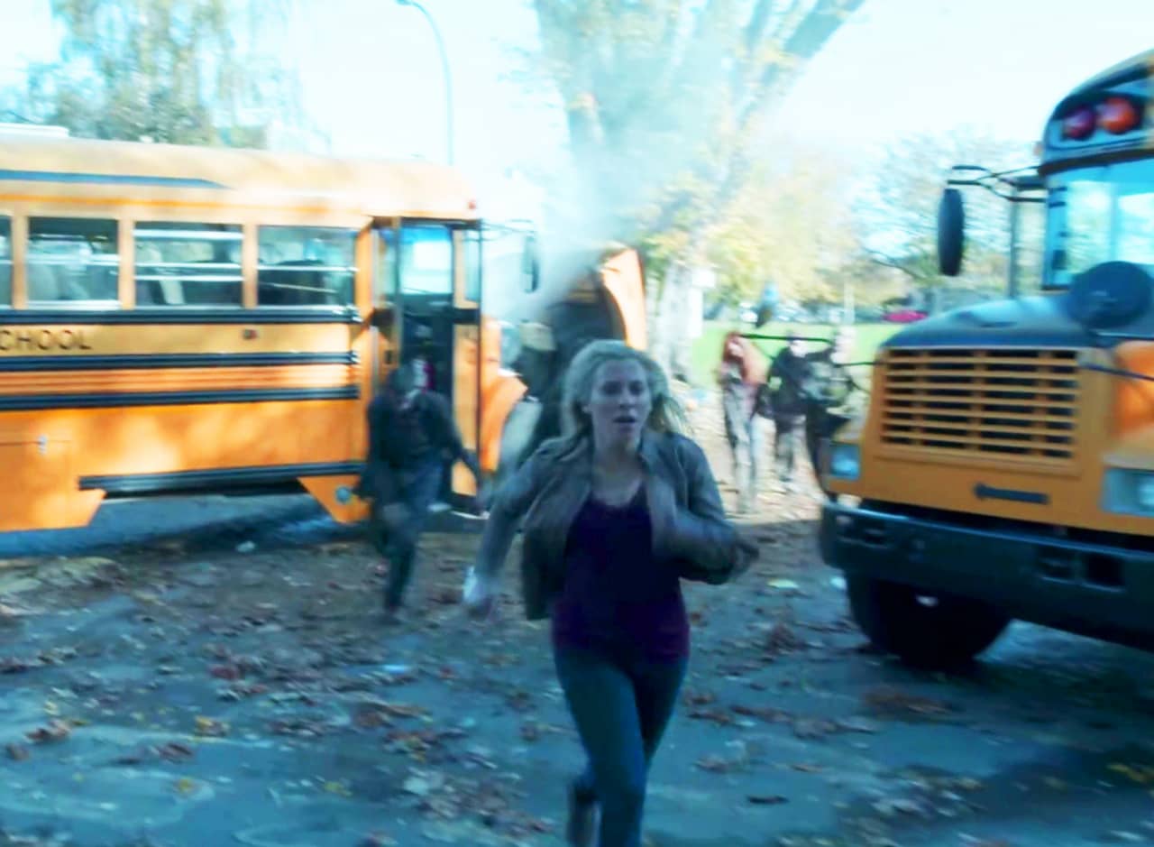 a teen girl runs past two school buses, zombies following close behind