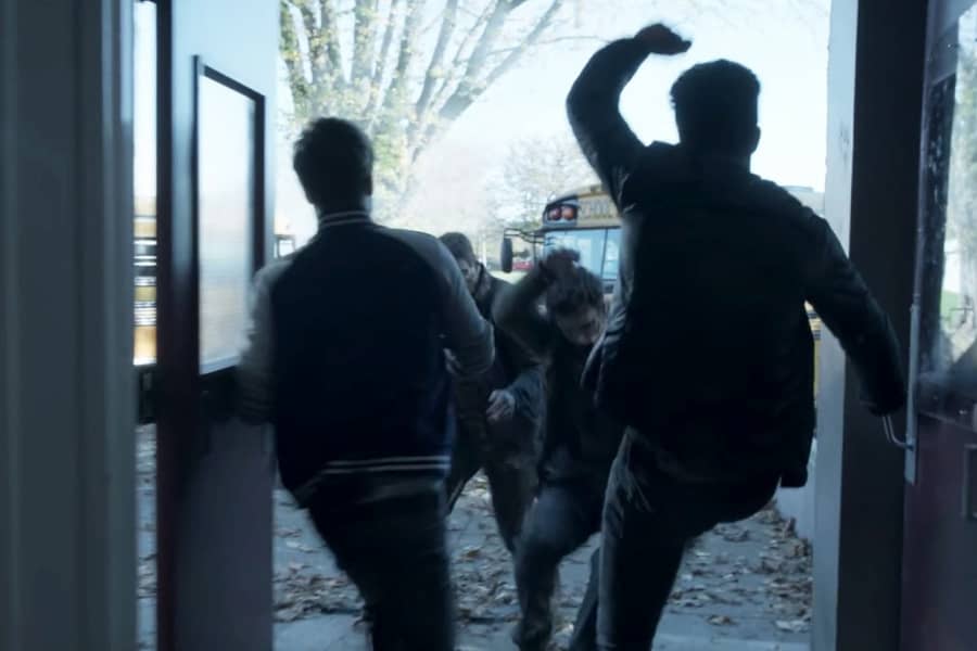 two teen boys kick zombies out a set of double doors